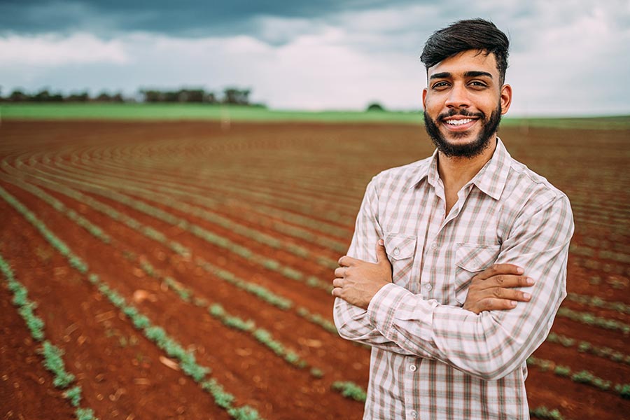 Specialized Business Insurance - Farmer Stands in Front of His Recently Planted Field, Arms Folded, Smiling